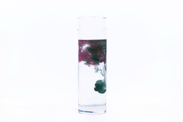 Green and pink paint fall in a glass with water