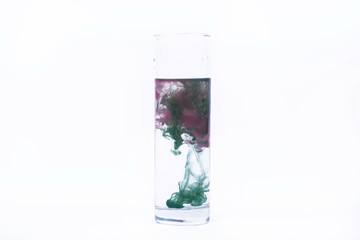 Green and pink paint fall in a glass with water