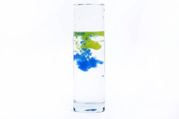 Blue and yellow paint fall in a glass with water