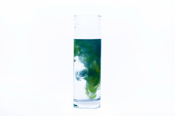 Blue and yellow paint fall in a glass with water
