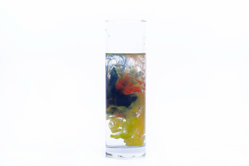 Blue, yellow, red paints fall in a glass with water
