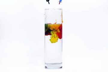 Blue, yellow, red paints fall in a glass with water
