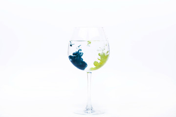 Wineglass with blue and yellow paints falling into it