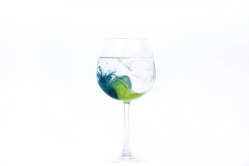 Wineglass with blue and yellow paints falling into it