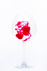 Pink paint falls in a wineglass with water