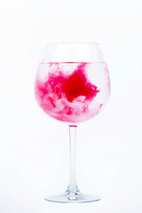 Pink paint falls in a wineglass with water