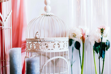 White bird cage stands before the flowers