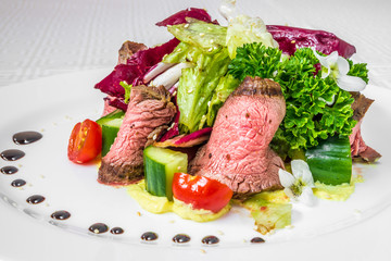 Tasty, appetizing pieces of sliced meat with sauce, tomatoes, cucumbers and herbs, on a white plate. Horizontal frame