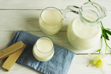 jug and glass of milk with a waffles on white wooden background.top view