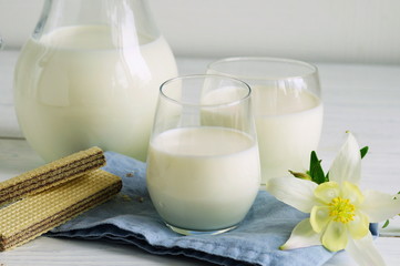 jug and glass of milk with a waffles on white wooden background
