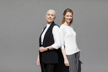 Two beautiful smiling women standing back ro back isolated on grey