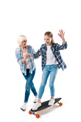 Fototapeta premium grandmother and happy granddaughter with skateboard isolated on white in studio