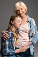 portrait of happy grandmother and granddaughter embracing isolated on grey in studio