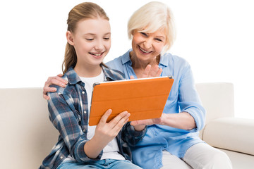 grandmother and grandchild using digital tablet and sitting on sofa isolated on white