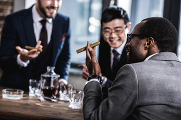 multicultural business team spending time, smoking cigars and drinking whiskey