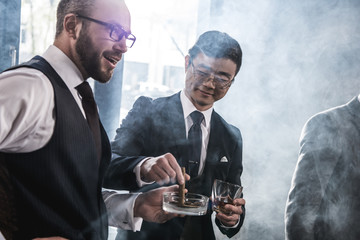 Multiethnic group of businessmen smoking and drinking whisky indoors, business team meeting