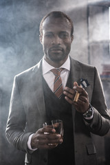 Confident african american businessman holding glass with whiskey and smoking cigar