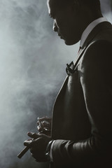 confident african american businessman in suit with glass of whiskey smoking cigar