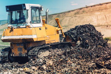 Industrial bulldozer pushing garbage and working on trash site