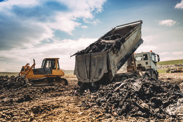 Dumping truck unloading garbage at dumping site. Industrial bulldozer, excavator and dumping trucks...