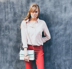 Portrait of a young woman dressed in a blouse, red Chino Trouser, a handbag turquoise on her...
