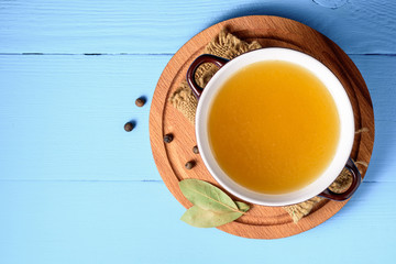 Chicken broth in ceramic bowl on blue wooden background.