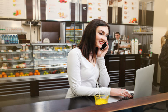 Young woman at a table and use her laptop in a cafe and talking by phone