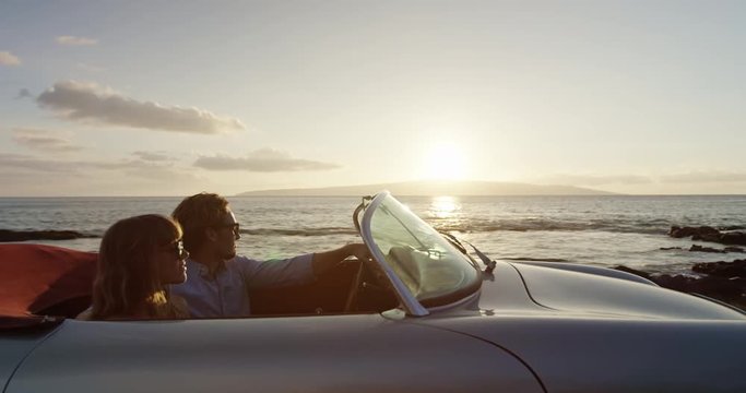 Romantic Couple Hands in thr Air Driving in Vintage Convertible Car at Sunset on Country Road by the Sea