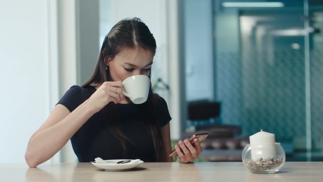 Beautiful girl drinking coffee and using phone in a cafe