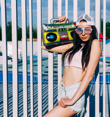 The old school. Style of 80 years. A stunning brunette girl in top and shorts posing on a warm summer evening with a ghettoblaster on her shoulder.