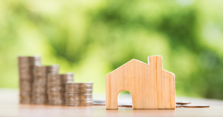 wooden house model and coins stacks on table, nature background, money, saving and investment concept