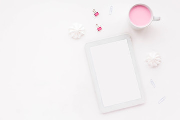 Woman's desk workspace with pink notebook, tablet, empty blank, pink yogurt, white pencil, candles and clips on white background. Top view, flat lay, copy space.