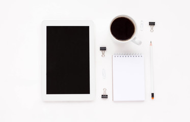 Office desk workplace with tablet, cup of black coffee, black clips, white notebook, empty blank, pencil on white background. Flat lay, copy space, top view