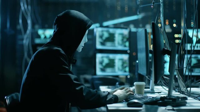 Masked Hacktivist Organizes Massive Data Breach Attack on Corporate Servers. They're in Underground Secret Location Surrounded by Displays and Cables. Shot on RED EPIC-W 8K Helium Cinema Camera.