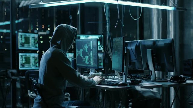 Hooded Hacker Breaks into Corporate Data Servers and Infects them with Virus. His Hideout Place has Dark Atmosphere, Multiple Displays, Cables Everywhere. Shot on RED EPIC-W 8K Helium Cinema Camera.