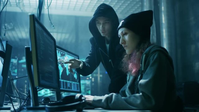 Team of Internationally Wanted Boy and Girl Hackers Organize Advanced Virus Attack on Corporate Servers. Place is Dark and Has Multiple displays. Shot on RED EPIC-W 8K Helium Cinema Camera.