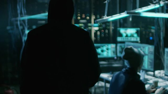 Hooded Hacker Takes His Place In At His Desk In Hacker's Lair. Place Is Neon, Dark And Has Many Displays, Shot On RED EPIC-W 8K Helium Cinema Camera.