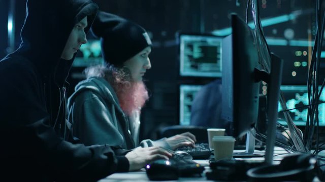 Team of Internationally Wanted Boy and Girl Hackers Organize Advanced Virus Attack on Corporate Servers. Place is Dark and Has Multiple displays. Shot on RED EPIC-W 8K Helium Cinema Camera.