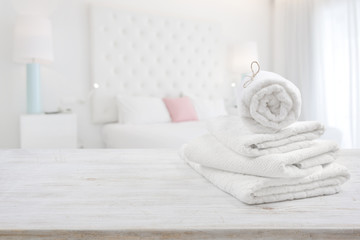 Fototapeta na wymiar White towels on wooden surface over blurred bedroom interior background