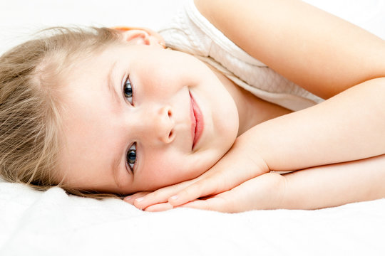 Pretty little blonde girl summer white dress lying on the floor and smiling at camera on white background.