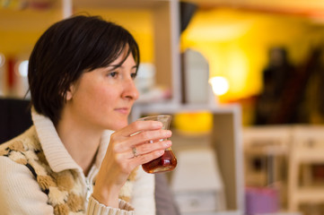 Delicate caucasian woman with short brown hair holding a glass of tea.