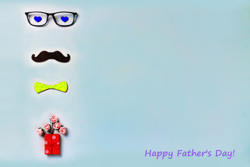 Happy Fathers Day inscription on a blue background. Black mustache, glasses, hipster yellow bow tie, small homemade box with a gift. Concept: Happy Fathers Day.