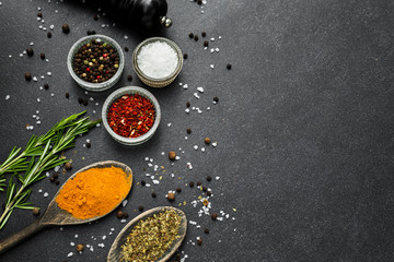 Close-up On a stone black spice surface, on a wooden spoon of turmeric, in glass pialls salt, paprika, dried basil, pepper mill, bottle with olive oil, rosemary, colorful, top view