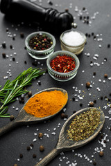 Close-up On a stone black spice surface, on a wooden spoon of turmeric, in glass pialls salt, paprika, dried basil, pepper mill, bottle with olive oil, rosemary, colorful, top view