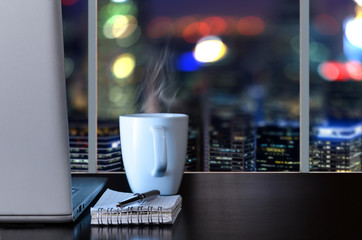 Laptop on table in office with panoramic night view of modern downtown skyscrapers at business district