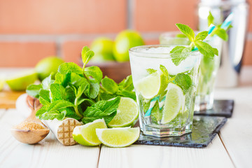Two fresh mojitos cocktail in glass on wooden table. Mojitos with mint leaves, lime and ice. Drink making tools and ingredients for cocktail.