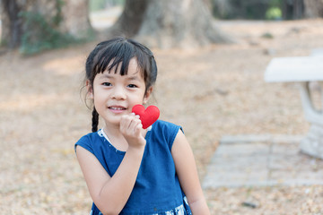 Asian kid holding a red heart in nature.
