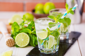 Two fresh mojitos cocktail in glass on wooden table. Mojitos with mint leaves, lime and ice. Drink making tools and ingredients for cocktail.