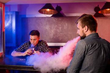 Two young men smoke electronic cigarettes in a vapebar