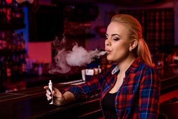 Young pretty woman smoke an electronic cigarette at the vape bar
